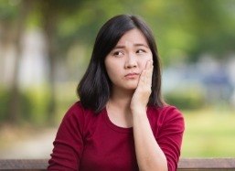 Woman with chipped and broken teeth holding cheek in pain