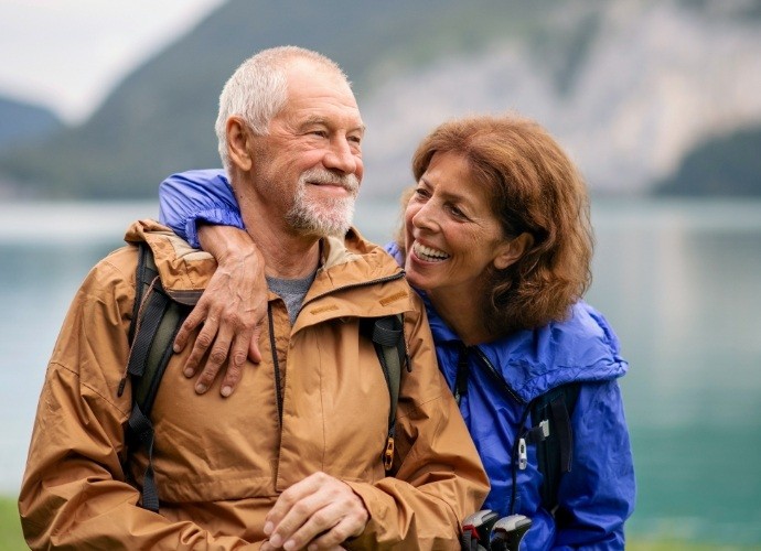 Older couple smiling together after tooth replacement with dental implants